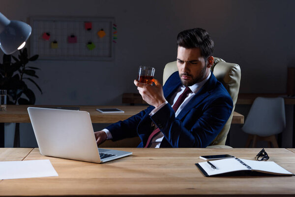 serious businessman sitting at laptop with glass of whiskey