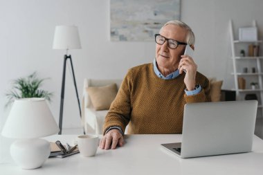 Senior confident man working in office and making phone call clipart