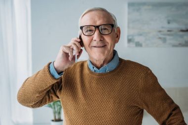 Yaşlı gülümseyen adam ofisinde çalışan ve telefon görüşmesi