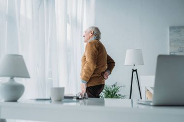 Senior man working in office suffering from back pain clipart