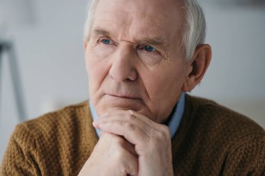 Senior thoughtful man leaning on hands in light room clipart