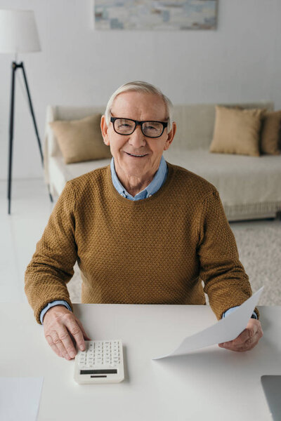 Senior confident man using calculator and holding blank paper