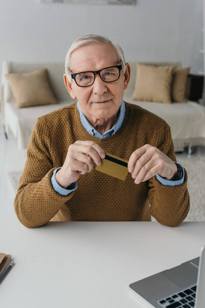 Senior confident man holding credit card by laptop