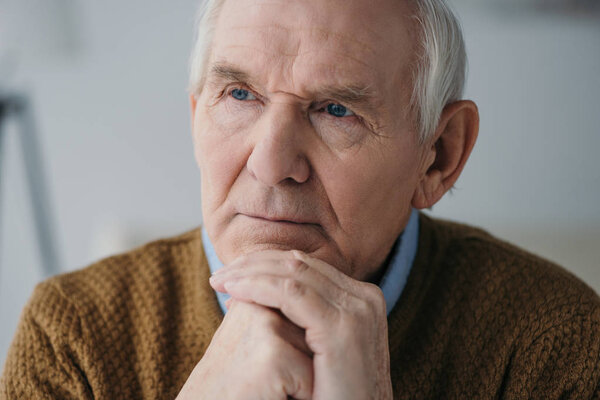 Senior thoughtful man leaning on hands in light room