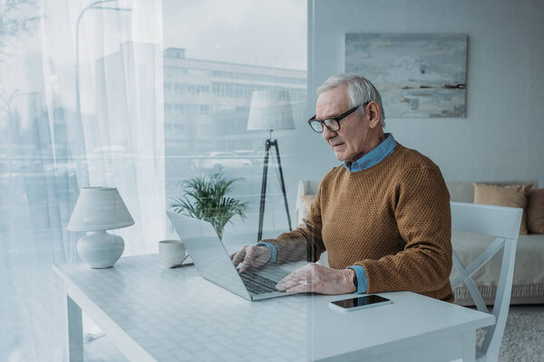 Behind the glass view of senior confident man working on laptop