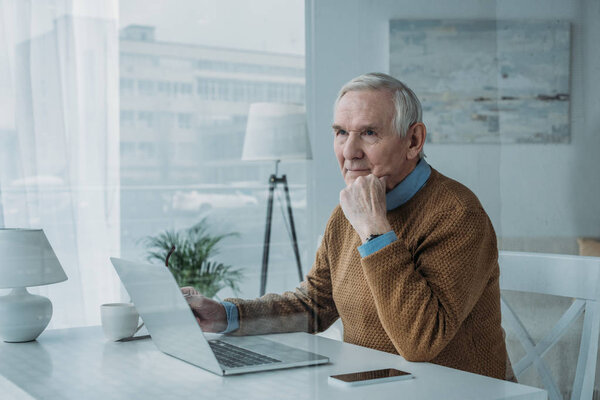 Behind the glass view of senior confident man working on laptop 