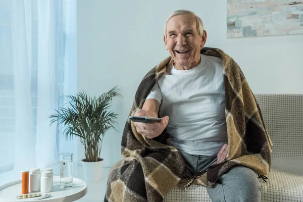 年配の男性で覆われている格子縞は ルームのテーブル上の薬では病気の時にテレビを見る — ストック写真