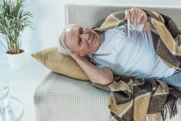 Senior Zieke Man Bedekt Met Plaid Ligt Bank Controleert Thermometer — Stockfoto