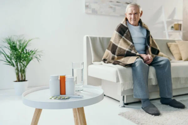 Senior Réfrigéré Homme Couvert Plaid Regarde Les Médicaments Sur Table — Photo