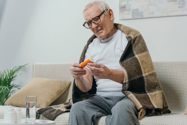 Senior man in eyeglasses and plaid looks at pill bottle
