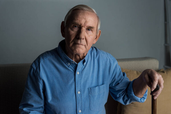 Senior confident man leans on a cane while sitting on sofa