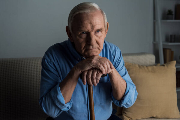 Tired senior man leans on a cane while sitting on sofa