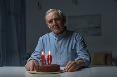 Senior lonely man celebrating 80 anniversary with cake and burning number candles clipart