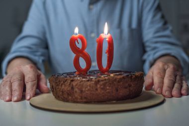 Close-up view of senior man celebrating 80 anniversary with cake and burning number candles clipart