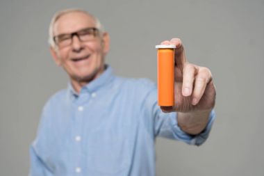 Senior smiling man holds blank bottle of pills isolated on gray background clipart