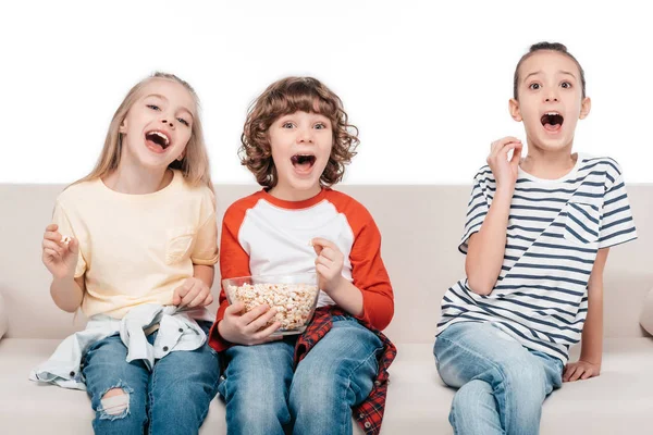 Cute children on couch with popcorn — Stock Photo