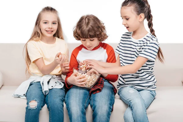 Cute children on couch with popcorn — Stock Photo
