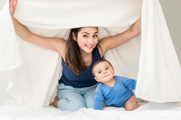 Mãe com seu filho brincando sob cobertor — Fotografia de Stock