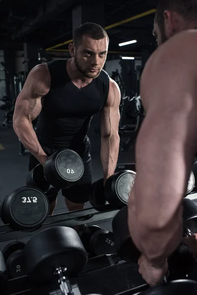Sportsman holding dumbbells while looking at mirror — Stock Photo