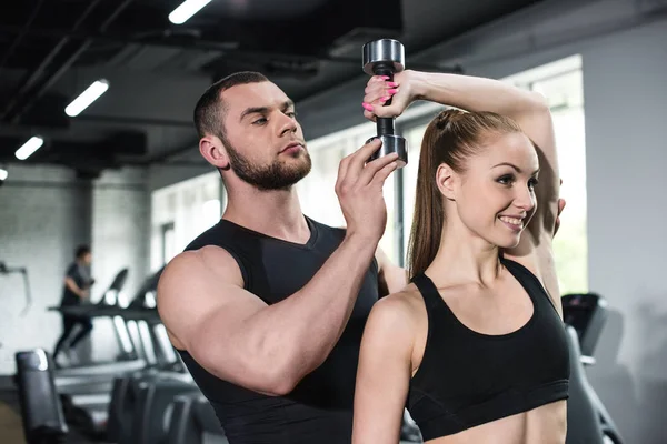 Ausbilder hilft junger Frau im Fitnessstudio — Stockfoto