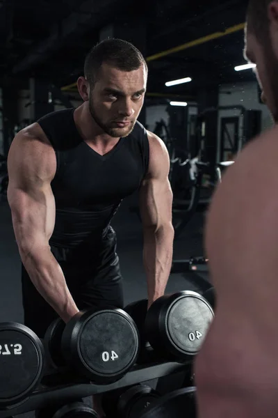 Sportsman holding dumbbells while looking at mirror — Stock Photo