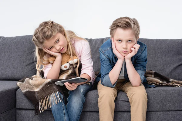 Bored brother and sister sitting on sofa — Stock Photo