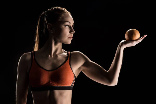 Menina desportiva pensativo segurando laranja — Fotografia de Stock