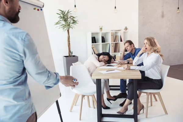 Empresário escrevendo no quadro branco enquanto colegas sentados — Fotografia de Stock