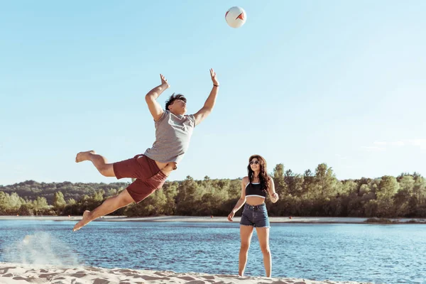 Amigos jugando voleibol en la playa de arena - foto de stock