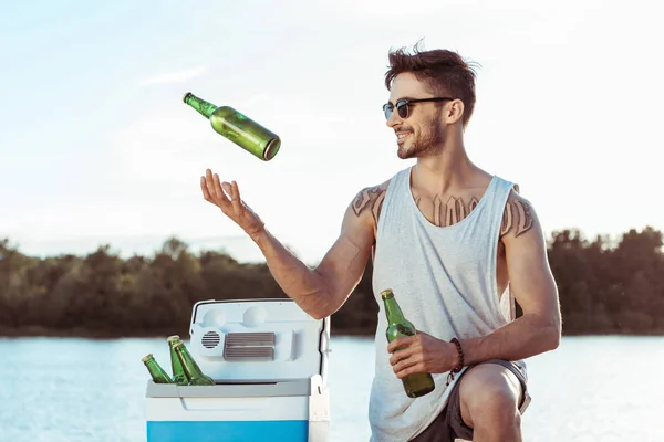 Чоловік жонглює пляшки пива на березі річки — стокове фото