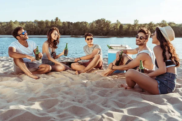Amigos beber cerveza mientras se relaja a orillas del río - foto de stock