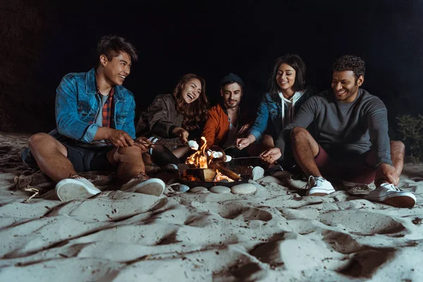 Multiethnic friends roasting marshmallows on bonfire — Stock Photo