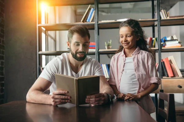 Chica leyendo libro con padre - foto de stock