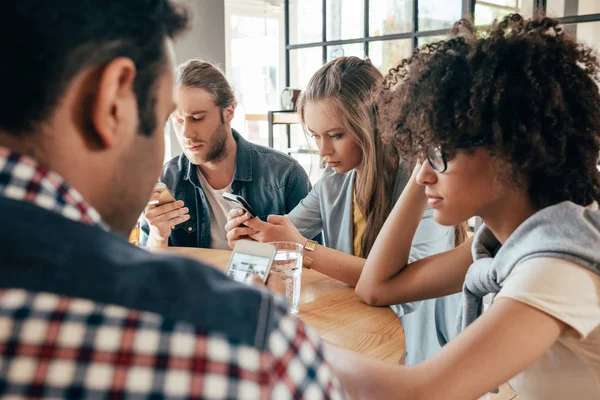 Amigos con dispositivos digitales en la cafetería - foto de stock