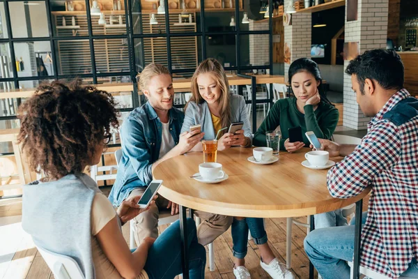 Amigos con dispositivos digitales en la cafetería - foto de stock