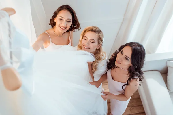 Novia con damas de honor tocando vestido de novia - foto de stock