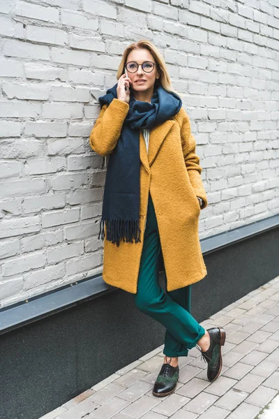 Жінка в жовтому пальто з смартфоном — стокове фото
