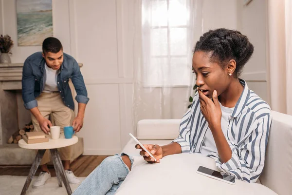 Mujer con teléfono inteligente y hombre poniendo tazas - foto de stock