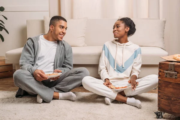 Casal comer pizza ao lado do sofá — Fotografia de Stock