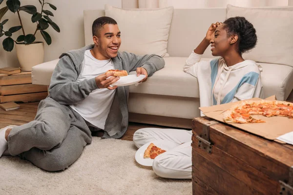 Couple eating pizza beside sofa — Stock Photo