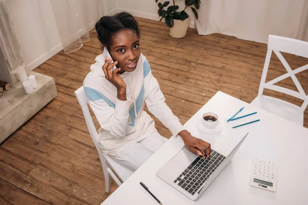 Mujer usando el ordenador portátil y hablando por teléfono - foto de stock