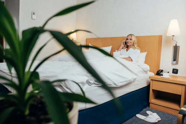 Attrayant mi-adulte femme parlant sur smartphone et regardant loin tout couché dans le lit à la chambre d'hôtel — Photo de stock