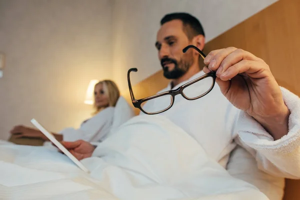 Close-up view of bearded mature man holding eyeglasses and using digital tablet in bed — Stock Photo