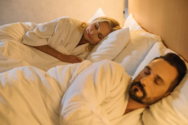 Beautiful mature couple in bathrobes sleeping together in bed in hotel room — Stock Photo