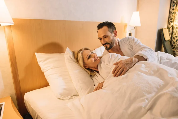 Belo casal adulto médio em roupões de banho acordar no quarto de hotel — Fotografia de Stock