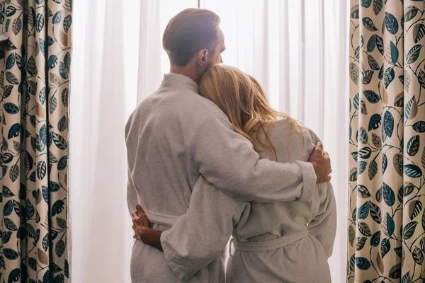 Vista trasera de pareja madura enamorada con albornoces y abrazos en la habitación de hotel - foto de stock