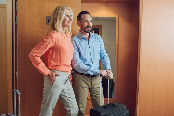 Feliz casal maduro com malas olhando para longe no quarto de hotel — Fotografia de Stock