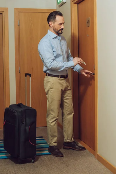 Homem barbudo com mala segurando cartão e abrindo a porta do hotel — Fotografia de Stock