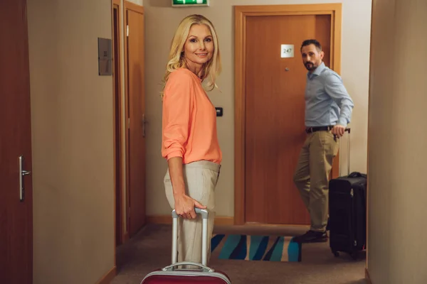 Middle aged couple with suitcases looking at camera on hotel corridor — Stock Photo