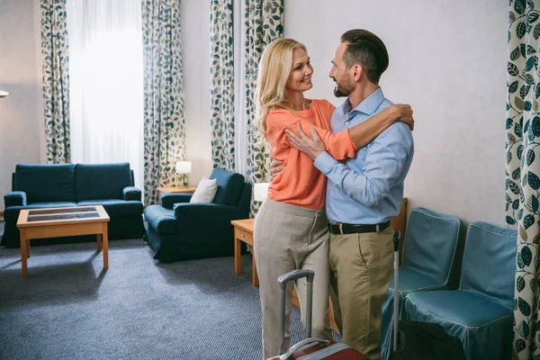 Glückliches reifes Paar umarmt, während es mit Koffern im Hotelzimmer steht — Stockfoto